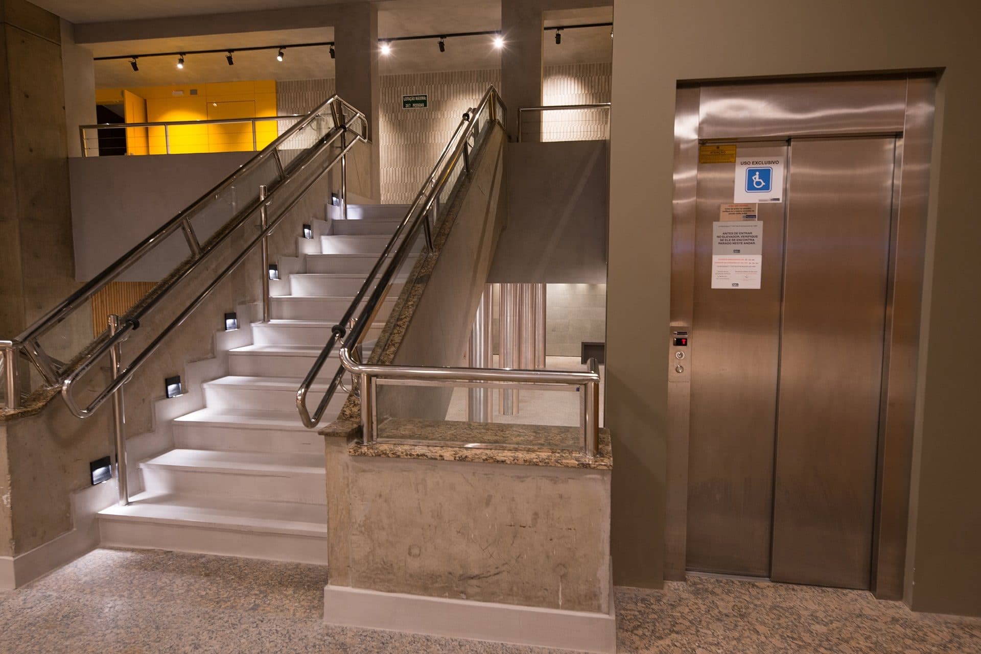 Escada com corrimão iluminado ao lado do elevador