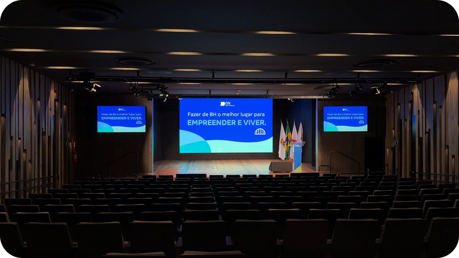 Auditório do Centro de Convenções durante um evento, com o palco e os telões acesos
