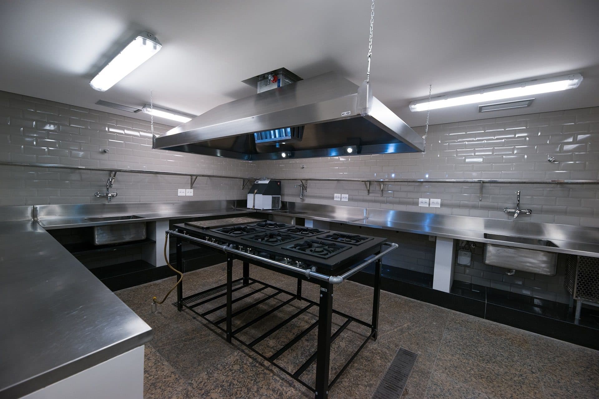 Cozinha de apoio com fogão industrial, bancadas de inox e coifa